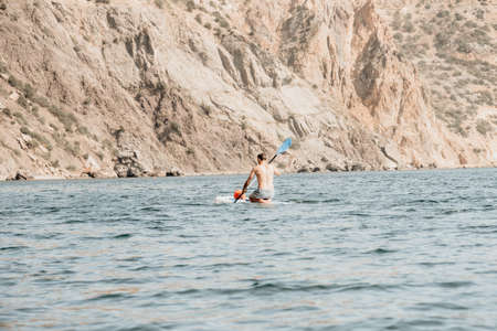 Side view foto of a man swiming and relaxing on the sup board. Sportive man in the sea on the Stand Up Paddle Board SUP. The concept of an active and healthy life in harmony with nature.の写真素材