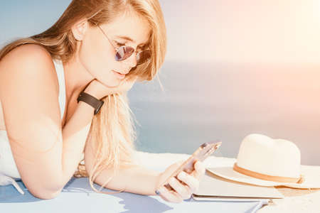 Digital nomad, woman in the hat, a business woman with a laptop sits on the rocks by the sea during sunset, makes a business transaction online from a distance. Freelance, remote work on vacation.の写真素材