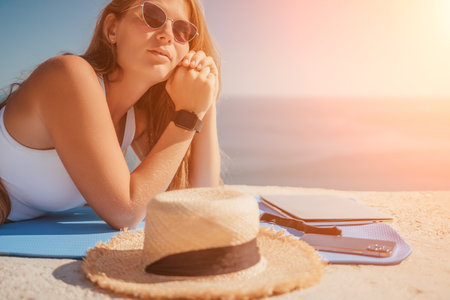 Digital nomad, woman in the hat, a business woman with a laptop sits on the rocks by the sea during...