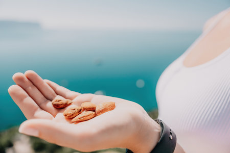 Young milky almond nuts in womans hand. A young caucasian woman eating fresh almond after morning fitness yoga near sea. Only hands are visibly. Healthy vegan food.の写真素材