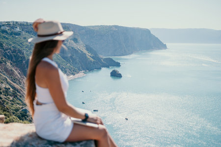 Digital nomad, woman in the hat, a business woman with a laptop sits on the rocks by the sea during sunset, makes a business transaction online from a distance. Freelance, remote work on vacation.の写真素材