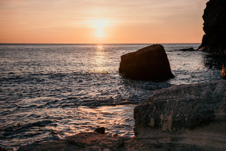 Sunset view on calm sea and volcanic rocky shores. Small waves on water surface in motion blur. Nature summer ocean sea beach background. Nobody. Holiday, vacation and travel conceptの写真素材