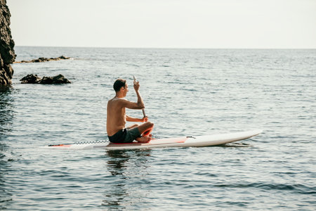 Side view foto of a man swiming and relaxing on the sup board. Sportive man in the sea on the Stand Up Paddle Board SUP. The concept of an active and healthy life in harmony with nature.の写真素材