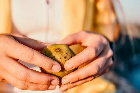 Womans hands opening a fig to eat. Fresh ripe fig fruit in the hands. A young woman eats figs on the beach, near sea. Ficus carica, Fig - green-yellow fruit. Close up. Selective focusの写真素材