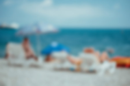 Abstract defocused blured summer and sea background. People relax on sun loungers under an umbrella...