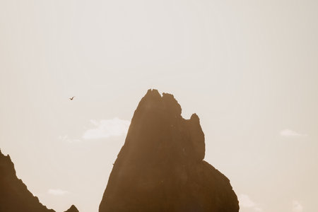 A red burning sunset over the sea with rocky volcanic cliff. Abstract nature summer ocean sea background. Small waves on golden warm water surface with bokeh lights from sun.の写真素材
