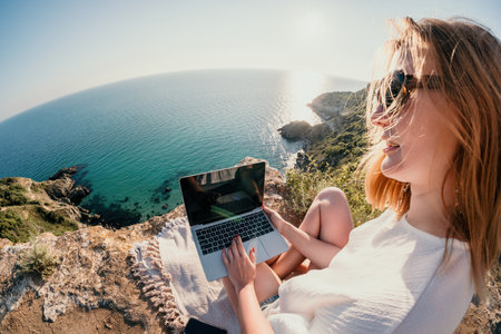 Woman sea laptop. Business woman working on laptop by sea at sunset. Close up on hands of pretty lady typing on computer outdoors summer day. Freelance, digital nomad, travel and holidays concept.の写真素材