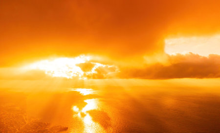 Aerial view red burning sunset over the sea with rocky volcanic cliff. Abstract nature summer sunset ocean sea background. Small waves on golden warm water surface Evening. Horizon. Nobody. No people.の写真素材