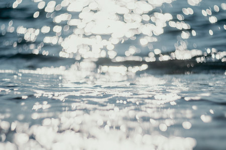 Abstract sea summer ocean sunset nature background. Small waves on golden water surface in motion blur with golden bokeh lights from sun. Holiday, vacation and recreational concept.の写真素材