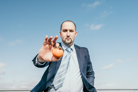 Man persimmon park. Hipster millennial man in a tie and jacket bites off a persimmon while sitting on a park bench in slow motion Young business people eat golden persimmons at lunchtime.の写真素材