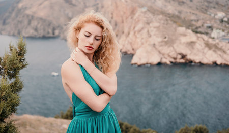 Redhead woman portrait. Curly redhead young caucasian woman with freckles looking at camera and smiling. Close up portrait cute woman in a mint long dress posing on a volcanic rock high above the seaの写真素材