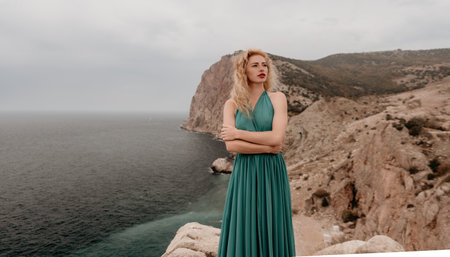Redhead woman portrait. Curly redhead young caucasian woman with freckles looking at camera and smiling. Close up portrait cute woman in a mint long dress posing on a volcanic rock high above the seaの写真素材