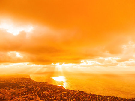 Aerial view red burning sunset over the sea with rocky volcanic cliff. Abstract nature summer sunset ocean sea background. Small waves on golden warm water surface Evening. Horizon. Nobody. No people.の写真素材