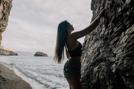 Sports Woman Climbing The Rock. Young woman With slim fit body climbing in volcanic basalt cave with beautiful sea view. The athlete girl trains in nature. Woman overcomes difficult climbing route.の写真素材
