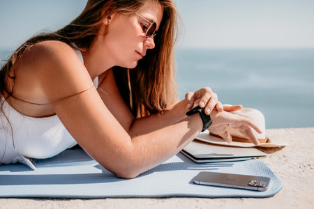 Digital nomad, woman in the hat, a business woman with a laptop sits on the rocks by the sea during sunset, makes a business transaction online from a distance. Freelance, remote work on vacation.の写真素材
