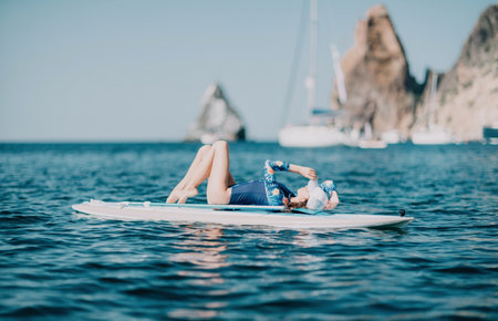 Woman sup yoga. Middle age sporty woman practising yoga pilates on paddle sup surfboard. Female...