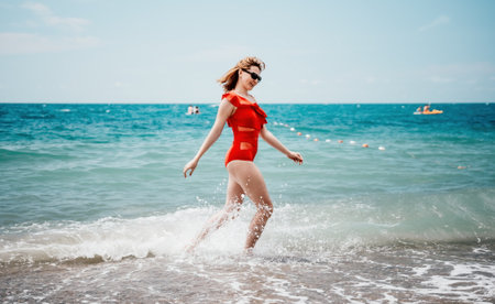 Young happy woman walks carefree on the seaside. Happy lady in red bikini. Portrait beautiful young woman relax smile around beach sea ocean in holiday vacation travel tripの写真素材