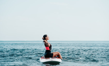 Sea woman sup. Silhouette of happy young woman in pink bikini, surfing on SUP board, confident paddling through water surface. Idyllic sunset. Active lifestyle at sea or river.の写真素材