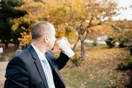 Mature entrepreneur drink coffee in autumn park. Senior executive rest in city park.の写真素材