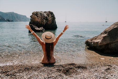 Woman travel sea. Happy tourist in hat enjoy taking picture outdoors for memories. Woman traveler posing on the beach at sea surrounded by volcanic mountains, sharing travel adventure journeyの写真素材