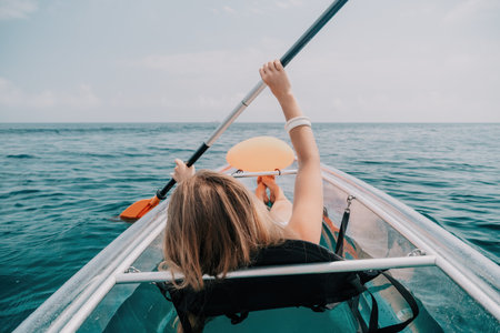 Woman in kayak back view. Happy young woman with long hair floating in transparent kayak on the crystal clear sea. Summer holiday vacation and cheerful female people relaxing having fun on the boatの写真素材