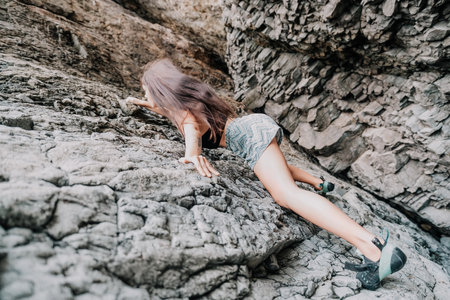 Sports Woman Climbing The Rock. Young woman With slim fit body climbing in volcanic basalt cave with beautiful sea view. The athlete girl trains in nature. Woman overcomes difficult climbing route.の写真素材