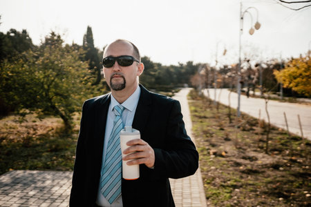 Mature entrepreneur drink coffee in autumn park. Senior executive rest in city park.