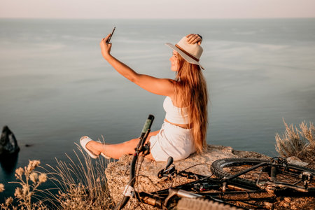 Woman travel sea. Happy tourist in hat enjoy taking picture outdoors for memories. Woman traveler posing on the beach at sea surrounded by volcanic mountains, sharing travel adventure journeyの写真素材