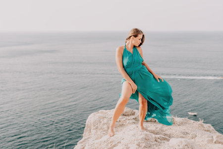 Woman travel portrait. Happy woman with long hair looking at camera and smiling. Close up portrait cute woman in a mint long dress posing on a volcanic rock high above the seaの写真素材
