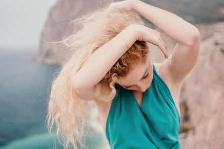 Redhead woman portrait. Curly redhead young caucasian woman with freckles looking at camera and smiling. Close up portrait cute woman in a mint long dress posing on a volcanic rock high above the seaの写真素材