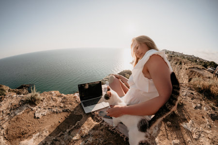 Woman sea laptop. Business woman petting cat and working on laptop by the sea. Close up on hands of pretty lady typing on computer outdoors summer day. Freelance, digital nomad and holidays concept.の写真素材
