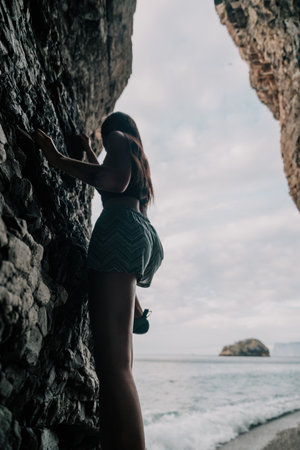 Sports Woman Climbing The Rock. Young woman With slim fit body climbing in volcanic basalt cave with beautiful sea view. The athlete girl trains in nature. Woman overcomes difficult climbing route.の写真素材