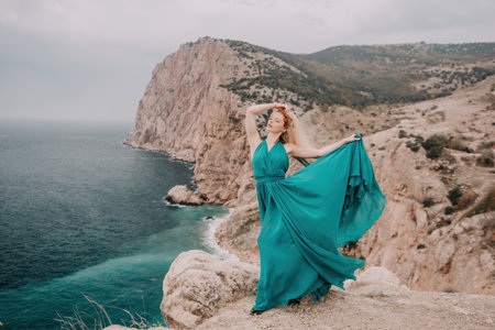 Redhead woman portrait. Curly redhead young caucasian woman with freckles looking at camera and smiling. Close up portrait cute woman in a mint long dress posing on a volcanic rock high above the seaの写真素材
