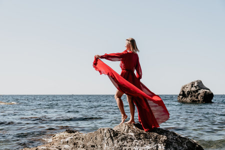 Woman travel sea. Happy tourist in long red dress enjoy taking picture outdoors for memories. Woman traveler posing on beach at sea surrounded by volcanic mountains, sharing travel adventure journeyの写真素材