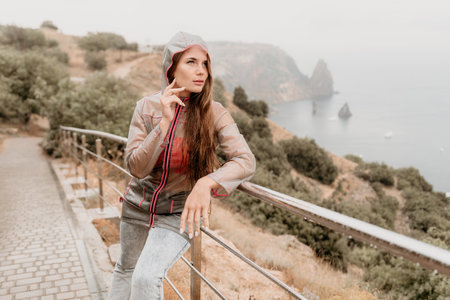 Woman rain umbrella. Happy woman portrait wearing a raincoat with transparent umbrella outdoors on rainy day in park near sea. Girl on the nature on rainy overcast day.の写真素材