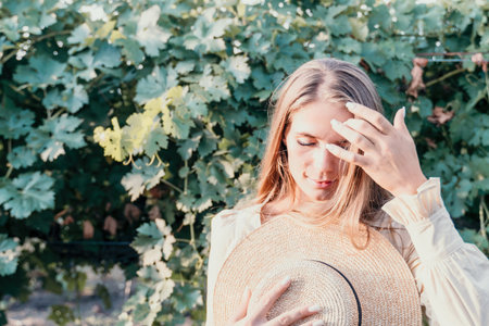 Woman at autumn winery. Portrait of happy woman holding glass of wine and enjoying in vineyard. Elegant young lady in hat toasting with wineglass smiling cheerfully enjoying her stay at vineyard.の写真素材