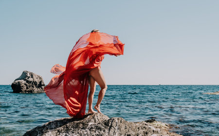 Woman travel sea. Happy tourist in long red dress enjoy taking picture outdoors for memories. Woman traveler posing on beach at sea surrounded by volcanic mountains, sharing travel adventure journeyの写真素材