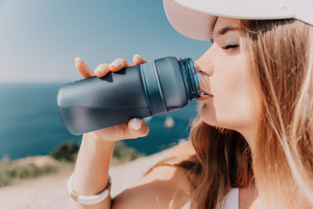 Fintess woman drinking water. Happy, active middle aged woman standing on beach and drinking water after excersise. Concept of lifestyle, sport. Close upの写真素材