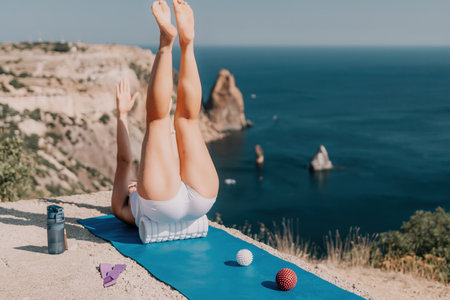 Woman sea pilates. Sporty happy middle aged woman practicing fitness on yoga mat with balls and roller near sea, smiling active female outside, enjoying healthy lifestyle, harmony and meditation.の写真素材