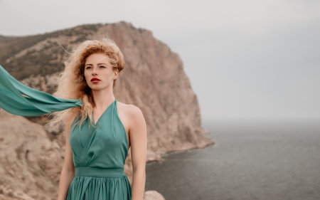 Redhead woman portrait. Curly redhead young caucasian woman with freckles looking at camera and smiling. Close up portrait cute woman in a mint long dress posing on a volcanic rock high above the seaの写真素材