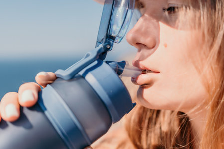 Fintess woman drinking water. Happy, active middle aged woman standing on beach and drinking water after excersise. Concept of lifestyle, sport. Close upの写真素材