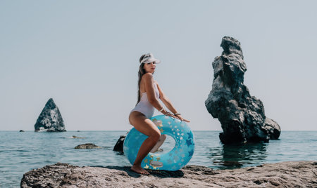 Woman summer sea. Happy woman swimming with inflatable donut on the beach in summer sunny day, surrounded by volcanic mountains. Summer vacation concept.の写真素材