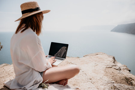 Woman sea laptop. Successful business woman working on laptop by the sea. Pretty lady typing on computer at summer day outdoors. Freelance, digital nomad, travel and holidays concept.の写真素材