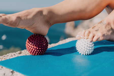 Woman sea pilates. Sporty happy middle aged woman practices pilates on yoga mat by the sea, using massage balls and roller near sea, smiling active female outside, enjoying healthy lifestyleの写真素材
