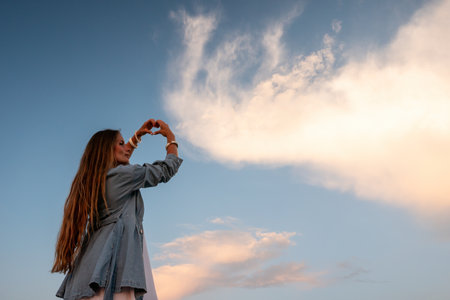 Happy woman standing with her back on the sunset in nature in summer with open hands. Romantic beautiful bride in white boho dress posing with mountains on sunsetの写真素材