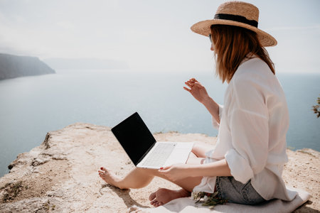 Woman sea laptop. Successful business woman working on laptop by the sea. Pretty lady typing on computer at summer day outdoors. Freelance, digital nomad, travel and holidays concept.の写真素材