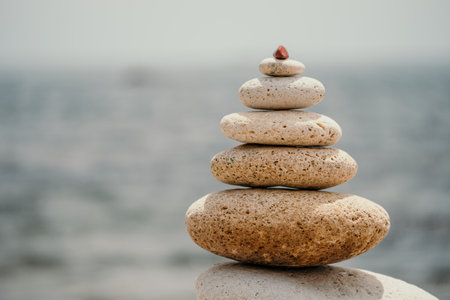 Pyramid stones on seashore with warm sunset on sea background for perfect holiday. Pebble beach and calm sea create a serene travel destination. concepts of happy vacation, meditation spa and calmnessの写真素材