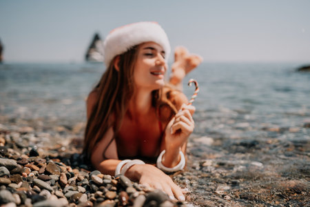 Woman travel sea. Happy tourist enjoy taking picture on the beach for memories. Woman traveler in Santa hat looks at camera on the sea bay, sharing travel adventure journeyの写真素材