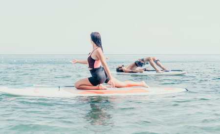 Woman man sup yoga. Happy young sporty couple practising yoga pilates on paddle sup surfboard. Female stretching doing workout on sea water. Modern family outdoor summer sport activity.の写真素材
