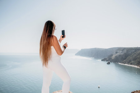 Digital nomad, woman in the hat, a business woman with a laptop sits on the rocks by the sea during sunset, makes a business transaction online from a distance. Freelance, remote work on vacation.の写真素材